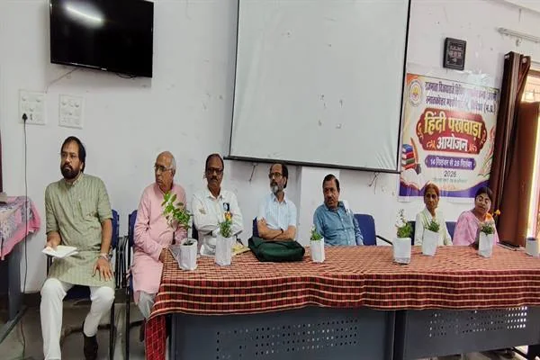 सभागार में मेज के पीछे बैठे अतिथि, सामने गमले और पीछे हिंदी पखवाड़ा आयोजन का पोस्टर